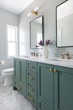 a white toilet sitting next to a green vanity in a bathroom with two mirrors above it