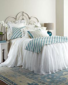 a white bed with blue and white pillows on it's headboard in a bedroom