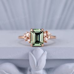 an emerald colored stone surrounded by pearls on top of a white cloth with a gold band