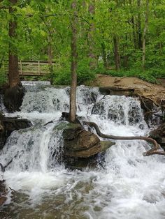 there is a waterfall in the woods with rocks and water running down it's sides