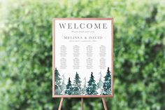 a welcome sign with trees on it in front of some bushes and greenery for an outdoor wedding