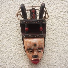 A dark brown chair crowns the head of this unusual smiling mask designed by West Africa's Christopher Nyasafo. Crafted from local sese wood and jute details the mask is called Ibiobio Horn named after a coastal people who live in southern Nigeria. Smiling Mask, Dark Brown Chair, Wood Mask, Brown Chair, African Home Decor, Expressionist Art, Beautiful Mask, African Masks, The Mask