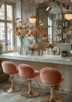 three pink chairs sitting in front of a bar with flowers on the counter and two mirrors