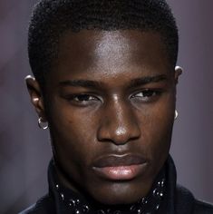 a close up of a person wearing a black shirt and bow tie with piercings on his ears