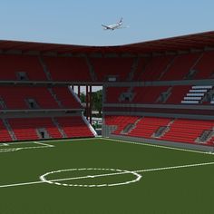 an airplane flying over a soccer field with red seats and green grass in the foreground