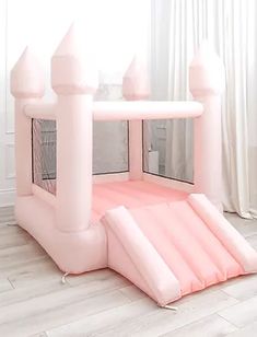 an inflatable pink castle is on the floor next to a white curtained window