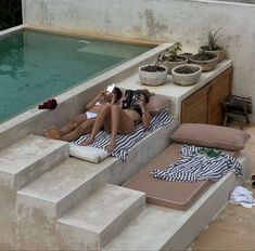 two women lounging on loungers in front of a swimming pool with their beverages