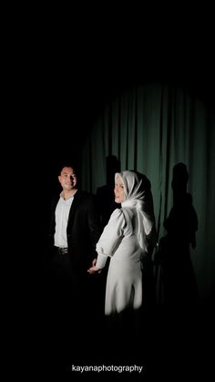 a man and woman standing next to each other in front of a dark background with curtains