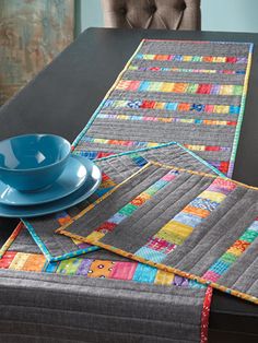 the table runner has been made with patchwork fabrics and is next to a blue bowl