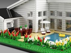 a lego model of a house with flowers in the front yard and lawn chairs on the other side