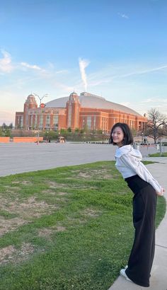 a woman is standing on the sidewalk in front of a large building with a clock tower