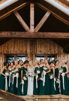 a group of women standing next to each other in front of a wooden building holding bouquets