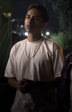 two men standing next to each other in the dark at night, one wearing a white t - shirt