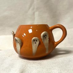 a ceramic cup with two ghost faces on it's side, sitting on a white surface