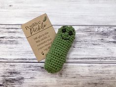 a green crocheted object sitting on top of a white wooden table next to a card