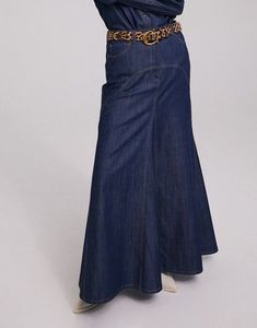 a woman is wearing a long denim skirt with a belt on the waist and has her hands behind her head