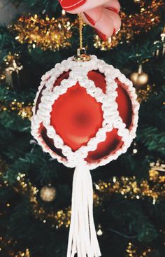 a hand holding a red and white ornament in front of a christmas tree