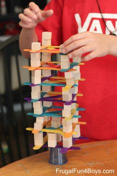 a young boy is playing with a tower made out of wooden sticks and colored strips