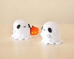 two crocheted ghost figurines with one holding an orange ball in its mouth