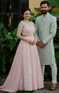 a man and woman standing next to each other in front of green plants wearing formal wear