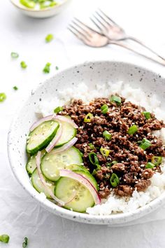 a white bowl filled with rice, cucumbers and meat on top of it