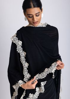 This elegant black knitted cape, crafted from a very soft 100% merino wool, combines warmth and refined designing. The delicate scalloped beige-colored filigree lace border creates a striking contrast against the black wool, adding a touch of sophistication and unique charm. Its soft, free-flowing silhouette makes it a versatile accessory. Whether for daytime outings or evening events, this timeless cape is designed to keep you stylishly cozy while making a bold statement. A must-have piece for Elegant Cashmere Shawl, Elegant Black Pashmina Shawl For Winter, Elegant Winter Pashmina Shawl, Elegant Black Pashmina Shawl For Formal Occasions, Elegant Black Dupatta Shawl, Elegant Winter Wool Pashmina Shawl, Elegant Lace Shawl For Winter, Elegant Lace Shawl Scarf, Elegant Winter Lace Shawl