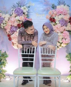 two people sitting on chairs in front of a floral backdrop