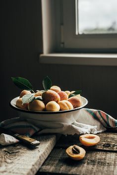 a bowl filled with fruit sitting on top of a wooden table next to a window