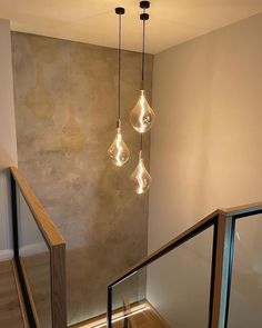 three light bulbs hanging from the ceiling in a room with wood flooring and handrails