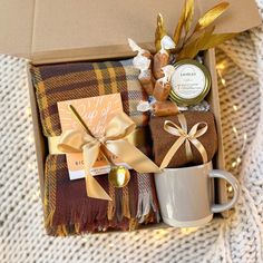 a gift box with coffee, cookies and other items on a tablecloth next to a mug