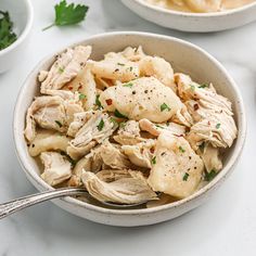 two bowls filled with food on top of a white table next to silver spoons