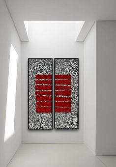 two abstract paintings in an empty room with white walls and floor, one is red