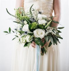 a bride holding a bouquet of white and green flowers