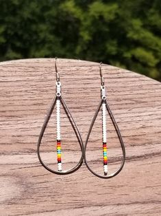 A teardrop shaped dangle earring with a beaded stem. Multicolor Teardrop Hoop Earrings With Dangling Beads, Long Drop Teardrop Earrings With Dangling Beads, Beaded Teardrop Dangle Earrings, Beaded Teardrop Earrings As Gift, Metal Teardrop Earrings With Pearl Drop, Beaded Teardrop Earrings For Gift, Bohemian Teardrop Earrings With Ear Wire, Adjustable Teardrop Dangle Earrings With Pearl Drop, Adjustable Metal Teardrop Earrings