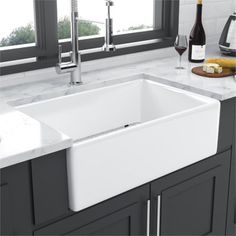 a white kitchen sink sitting under a window next to a counter top with wine bottles