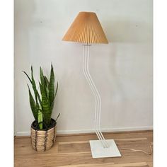 a lamp that is next to a potted plant on the floor in front of a wall