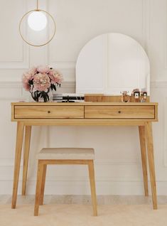 a wooden desk topped with a mirror and a vase filled with flowers next to a stool