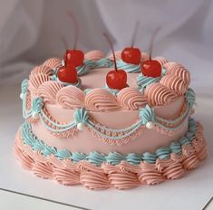 a pink cake with blue icing and cherries on top is sitting on a table