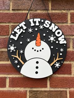 a sign that says let it snow on the side of a brick wall with a snowman