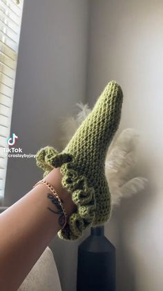 a woman's hand wearing a green crocheted mitt with feathers on it