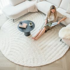 a woman sitting on the floor reading a book in front of a white sectional couch