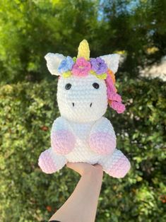 a hand holding up a crocheted stuffed animal with a unicorn on it's head