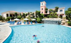 people are swimming in an outdoor pool with umbrellas and lounge chairs around the pool