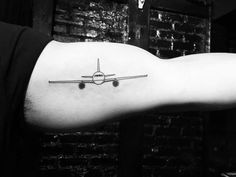 a black and white photo of an airplane tattoo on the left arm, which is attached to a man's right arm