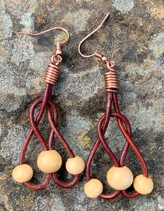 two pairs of brown and white beads are hanging from red leather earwires on a rock