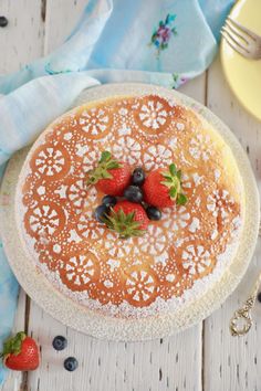 a cake on a plate with berries and blueberries in the middle, sitting on a white wooden table