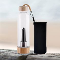 an empty glass bottle with a wooden cap next to a small black bag on a rock