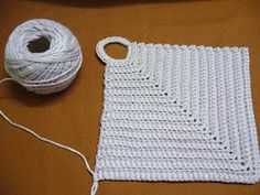 a white crochet blanket next to a ball of yarn on top of a table