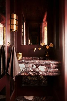 a bathroom with red walls and marble counter tops, gold accents on the mirror above the sink