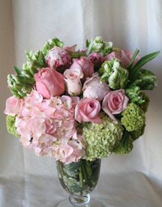 a vase filled with pink and green flowers on top of a white cloth covered table